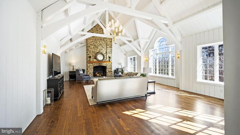 light filled family room with white walls and ceiling, exposed beams, stone floor to ceiling fireplace hardwood floors