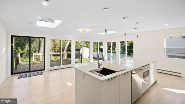 bright kitchen with center island, light hardwood floors, sliding doors to deck with trees and grass in yard