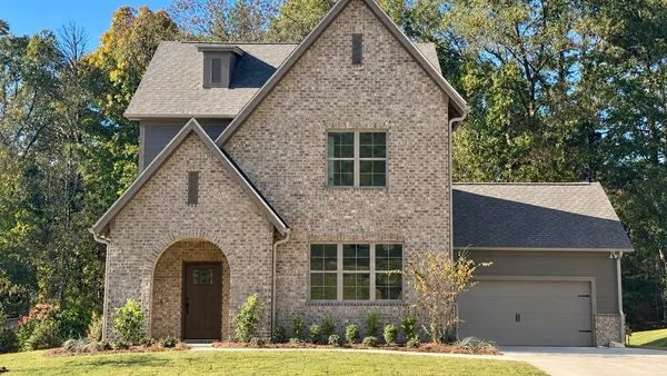 Multi-story brick exterior featuring a recessed arched entryway, steeply pitched rooflines, and a side-load garage