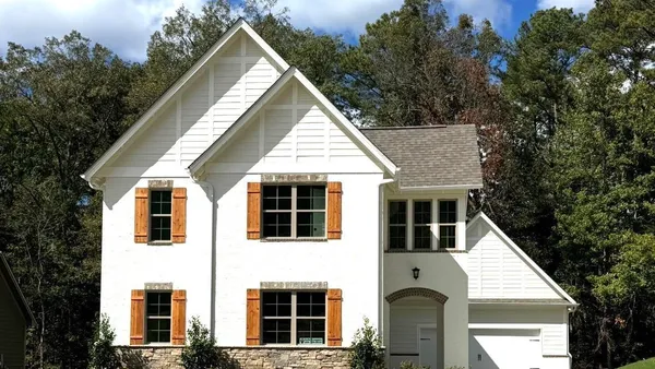 Two-story exterior featuring painted brick, stacked stone veneer, wood-finish shutters, decorative gable accents, and a concrete driveway