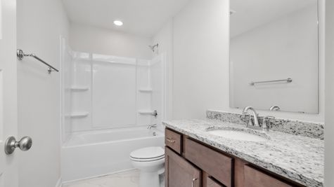 Interior photo of secondary bathroom with brown cabinets and granite counter tops