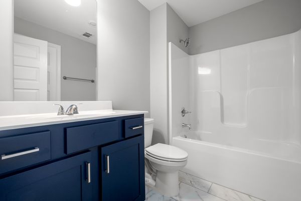 Interior view of secondary bathroom with blue cabinets, white countertop, and tub/shower combo