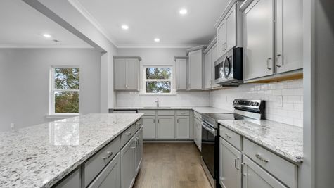 Interior photo of kitchen with gray cabinets and white tiled backsplash with a granite countertop