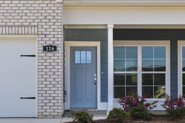 Exterior photo of front door with grayish blue siding, same colored front door and white brick