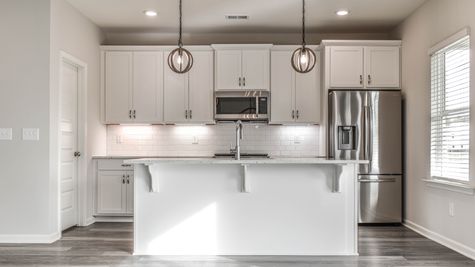 Interior view of all white kitchen with large island and pendant lights