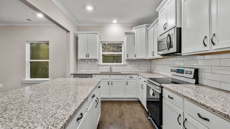 Interior photo of kitchen with white cabinets and white tiled backsplash with a granite countertop