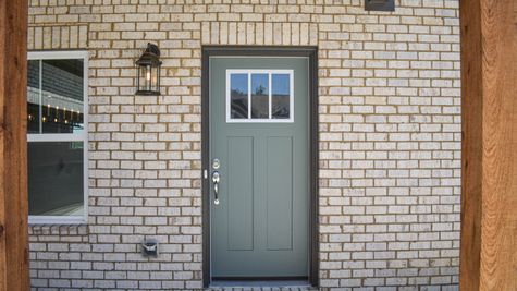 Exterior view of green front door with white brick and cedar posts