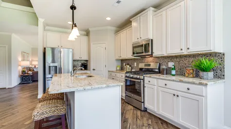The Jasmine model home kitchen with white cabinets, island with pendant lights, granite counters, wood floors.
