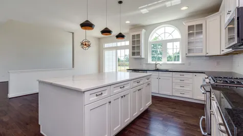 Baldwin kitchen with large island, white cabinets, decorated arched transom window over sink, slider door to outside.