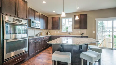Oakton Kitchen with dark cabinets, stainless steel appliances, double wall oven, hanging pendant lights over island, slider door to back yard.