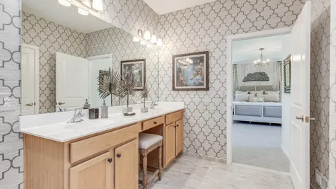 Master bedroom bathroom with double sink vanity in Zinnia model home decorated with wallpaper.