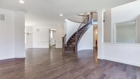 Curved stair case in front hall of The Stoneleigh luxury home model, with dark hardwood floors & stairs, decorative handrail.