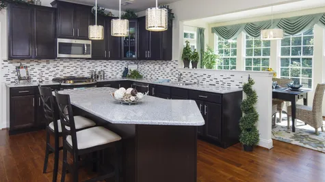 Baldwin model home kitchen with island, granite countertops, dark cabinets, pendant lights over island.