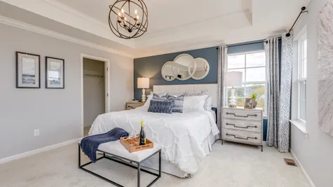 The owner's bedroom in the new construction townhome shown with a tray ceiling and accents of navy blue and grey within the decor.