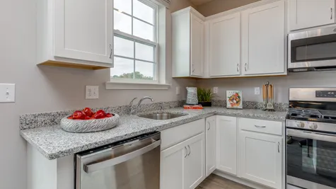 New townhome kitchen shown with white cabinets and grey toned granite counter top and stainless steel appliances.