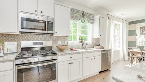 Kitchen in Zinnia model home with white cabinets, wood floors, stove + oven with microwave above.