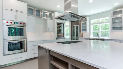 Stoneleigh Gourmet Kitchen with double wall oven, large cook top & large stainless steel exhaust hood, white cabinets.