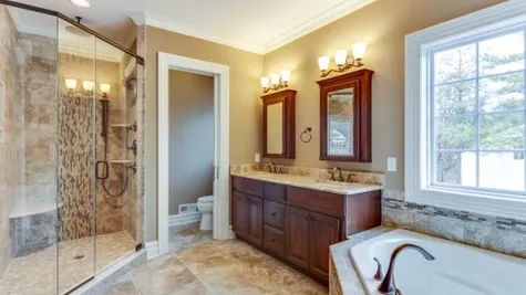 The Stoneleigh Master Bathroom with soaking tub, walk-in shower with glass door, double sink vanity with mirrored cabinets above.