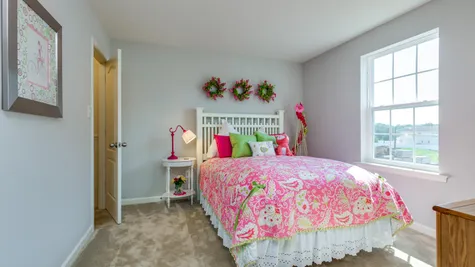 Bedroom in The Laurelton model home decorated with sample furniture for a girl, with carpet and window.