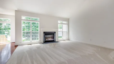 Augusta new home gathering room/family room with pale carpet, fireplace and large windows with transoms.