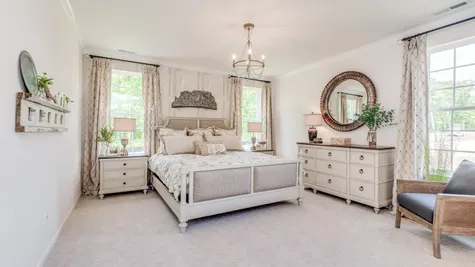 Master bedroom in Zinnia model new home with pale carpets, three large windows and sample furniture.