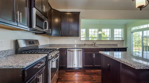 The Wexford Kitchen with dark cabinets, stainless steel appliances, and breakfast nook with sliding glass door beyond.