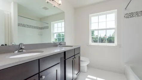 Badwin hall bath with shower over tub and double sink vanity.
