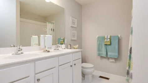 Laurelton bathroom with double sink vanity, mirror, lights above, toilet, shower over tub on right.