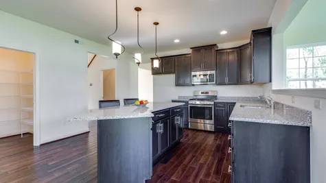 The Wexford model new home kitchen with dark cabinets, island, wood floors, handing pendant lights, pantry.