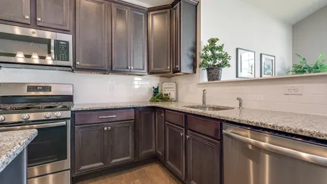 Kitchen of the Laurelton model new home in NJ with dark cabinets, white tile backsplash, wood floor, granite counters.