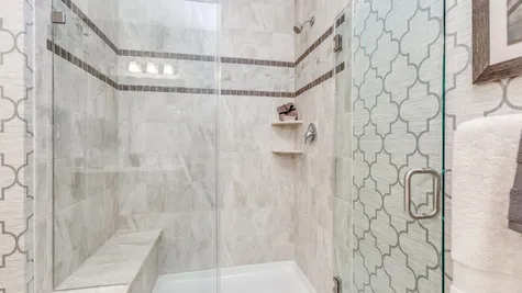 Walk-in shower in master bedroom bathroom in Zinnia model new home with decorative tile, glass doors.