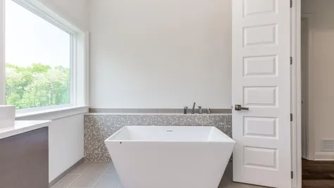 The Stoneleigh Master Bathroom with modern, white, simple, rectangular soaking tub and window above.