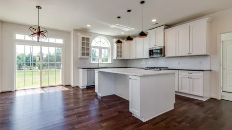 Baldwin model kitchen with white cabinets, granite counters, large island, eating area and slider doors to outside.