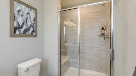 The shower within the owner's bathroom is shown with tan tile walls and decor in navy blue & gold accents.