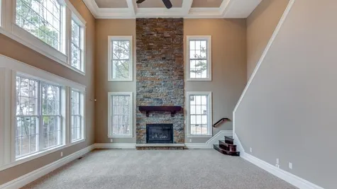 Two story Stoneleigh family room with stone fireplace, many two story high windows, back staircase to second floor.
