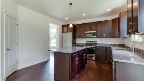 Kitchen of the Ashton model home with dark cabinets, central island and wood floor.