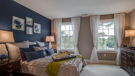 A bedroom in Brandywine model new home with two large windows, carpet and sample furniture.