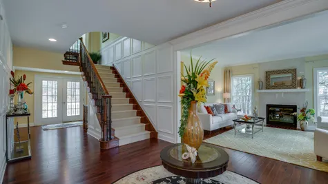 Front hall of Brandywine luxury model home with flower arrangements, stairs in view and formal living room to right.