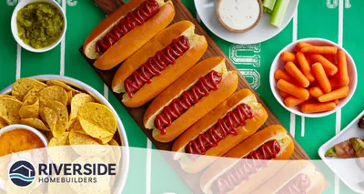 Image of a line of hot dogs and bowls of relish, tortilla chips, carrots and veggie dip.