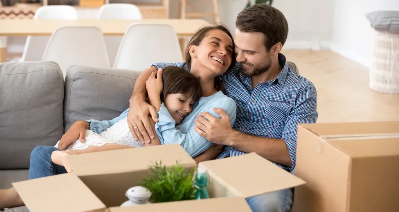 Two parents and child laying on couch next to a moving box.