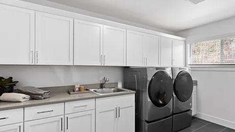 laundry room with cabinet storage, front load washer/dryer and utility sink