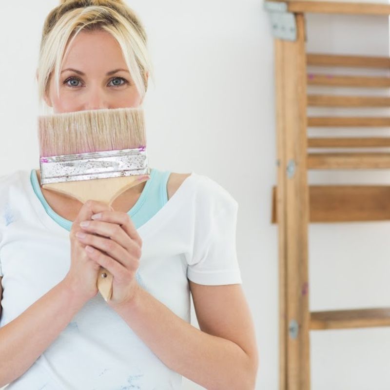 A woman holding a paintbrush, representing the yearly home maintenance checklist of custom home builder Robertson Homes in Michigan