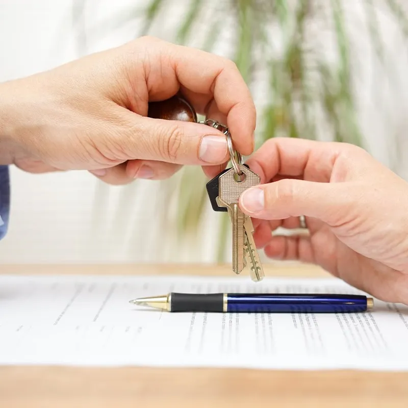 A person handing keys to another person representing the process of buying a home