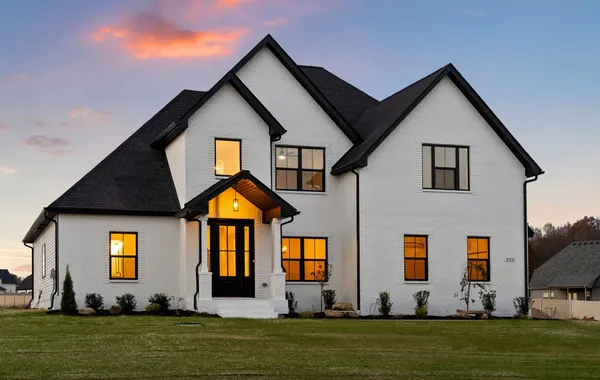 Front exterior of The Stella by Rockwood Homes, a two-story white home with black trim and a timber-frame entry, at dusk.