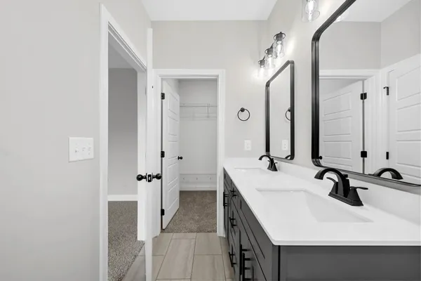 The Cumberland primary bathroom with a dark gray double vanity, black fixtures, and a view to the walk-in closet