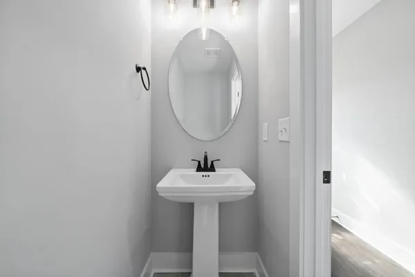 The Maui half bath with a white pedestal sink, an oval mirror, and a wall sconce