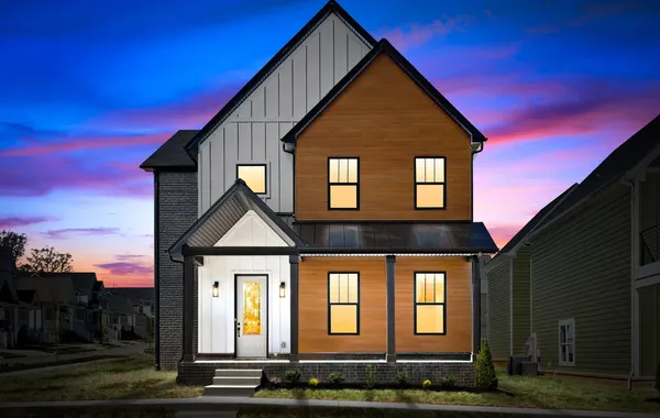Front exterior of The Riverside by Rockwood Homes, a two-story home with white board and batten and wood siding, at dusk.