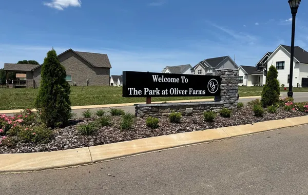 Welcome sign at the entrance to The Park at Oliver Farms by Rockwood Homes in Clarksville, TN, with homes behind it.