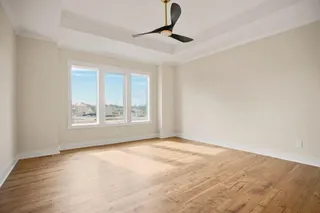 Tray ceiling with crown molding, contemporary ceiling fan, three large windows, wood-finish flooring, and neutral wall tones