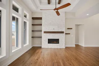 Expansive room featuring wood-finish flooring, a contemporary fireplace with a stone surround, and built-in shelving